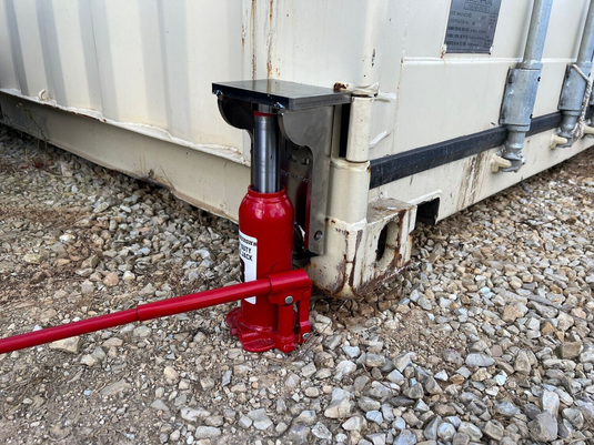 EZY Lift in use leveling a shipping container with a red bottle jack (bottle jack not included).
