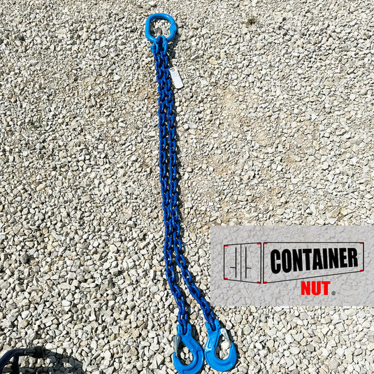 A Chain Sling from Container Nut, featuring a blue chain with two hooks and a circular ring, is laid out on a gravel surface. A partially visible label is attached to the chain.