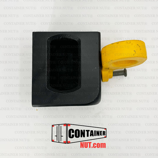 A Bottom Lifting Lug from Container Nut. A ISO corner casting has a smooth, rounded yellow hook attached to one corner. The corner casting includes a rectangular hole on the top side and a circular hole on the front side. The hook is designed to pivot from the corner, indicating its mechanical purpose.