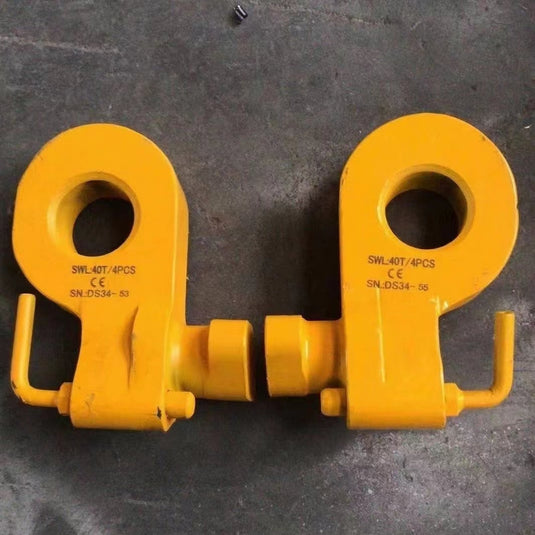 Two yellow Bottom Lifting Lugs from Container Nut, heavy-duty and featuring CE markings with serial numbers ("SWL40T/4PCS SN-DS34-53" and "SWL40T/4PCS SN-DS34-56"), lie on a gray surface. The lugs have large circular openings and pinned shaft fittings.